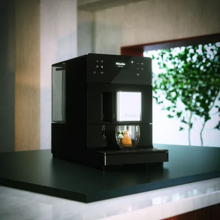 Modern Miele coffee machine on a sleek countertop with soft lighting and greenery in the background.