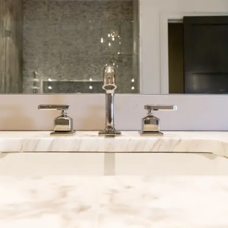 Close-up of a modern bathroom sink with sleek chrome faucets and a marble countertop.