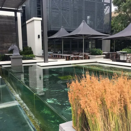 Modern outdoor seating area with umbrellas beside a reflective water feature and ornamental grasses.
