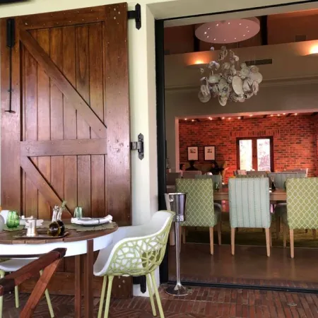 Cozy dining area with rustic wooden door, modern chairs, and a chandelier over a large table inside a brick-walled room.