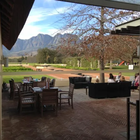 Outdoor patio with wooden and cushioned seating overlooking a garden and mountain landscape under blue sky.