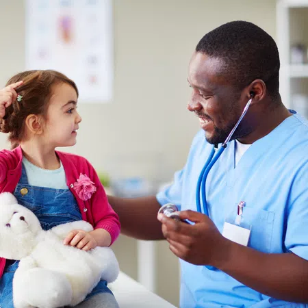 Child holding teddy bear with doctor using stethoscope, smiling during pediatric checkup in medical office.
