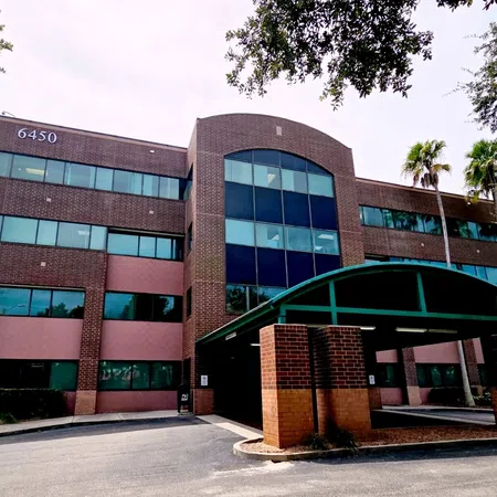 Modern three-story office building with brick facade, large windows, and a covered entrance under clear skies.