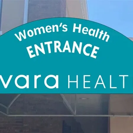 Blue curved awning with Women's Health Entrance and evara Health logo above building entrance on a sunny day