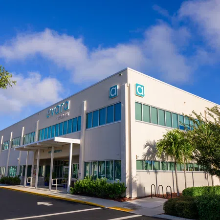 Modern two-story commercial building with large windows under a blue sky and landscaped greenery around.