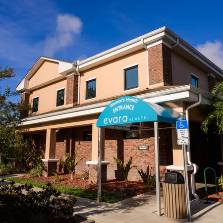 Exterior view of Evara Health women's health clinic entrance with blue sky and greenery outside.