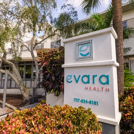 Evara Health clinic sign with contact number surrounded by greenery outside a modern building on a sunny day
