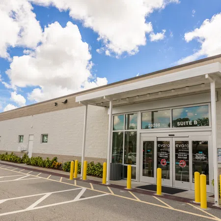 Exterior view of a modern commercial building entrance labeled Suite B with yellow bollards and a blue sky.