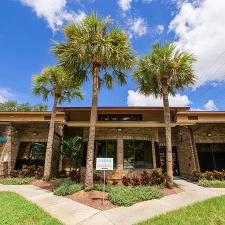 Single-story brick commercial building with palm trees, blue sky, and landscaped front garden under bright sunlight