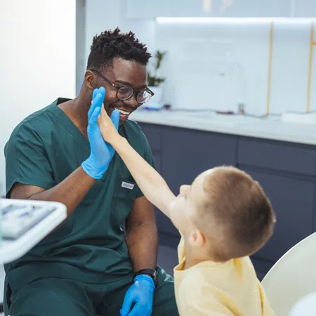 Smiling dentist giving high five to young boy in dental clinic chair during appointment