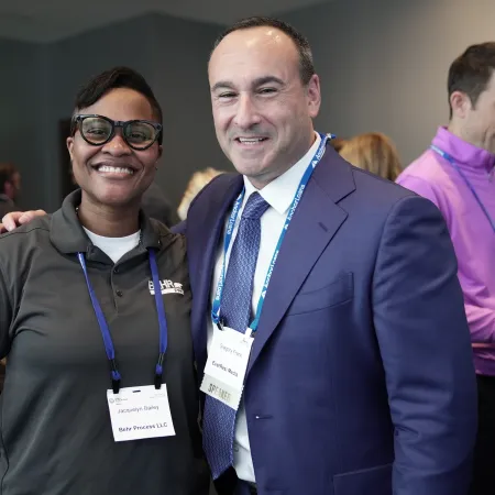 Smiling professionals at a networking event wearing name badges and business attire, engaging and posing for photo.