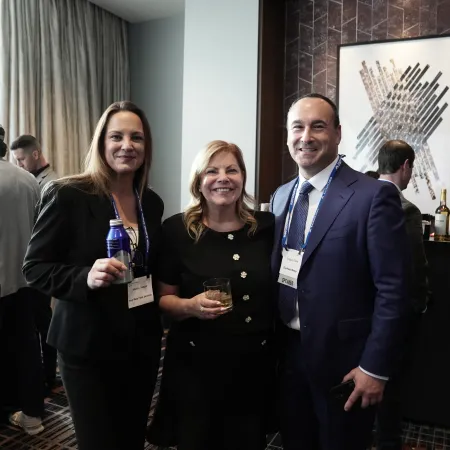 Three professionals smiling at a networking event with drinks in hand inside a modern conference room.