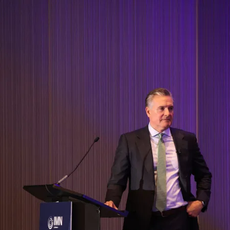 Man in a suit standing at a podium with IMN Build-to-Rent Spring banner against a purple background.