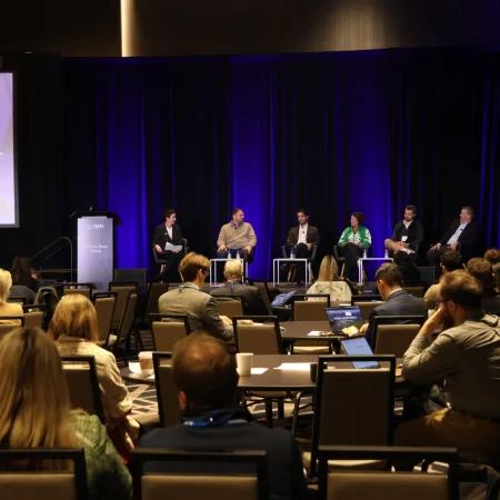 Panel discussion at a business conference with audience seated and dark blue stage curtains.