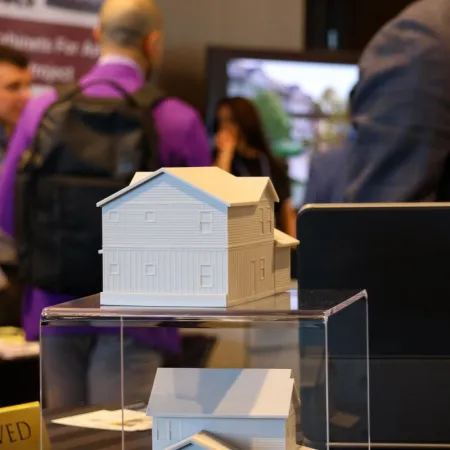 White architectural house models on clear display cases at a real estate event with attendees in the background