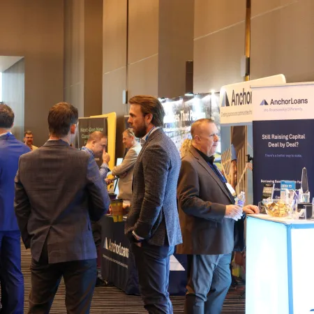 Business professionals networking and discussing at a conference with Anchor Loans booth in background