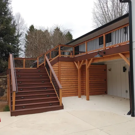 Modern wooden deck with stairs leading to upper level and red closed patio umbrella on concrete patio.