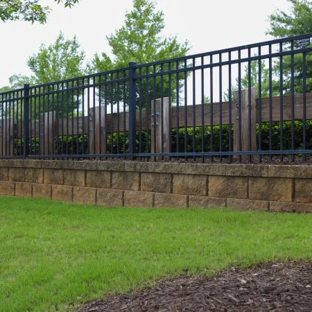 Black metal and wood fence on a stone retaining wall with green grass and trees in background