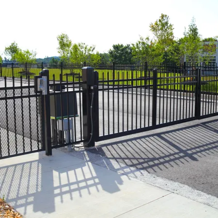 Automated black metal security gate with keypad access at a parking lot entrance on a sunny day.