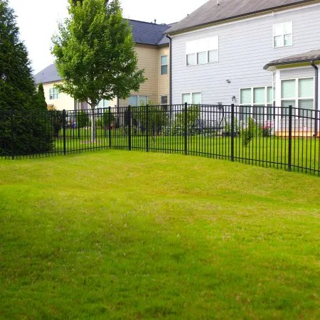 Green backyard with trimmed grass surrounded by black metal fence and houses in the background on a sunny day