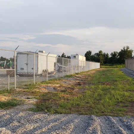 a fenced off area with a wire fence and a field with a building in the background