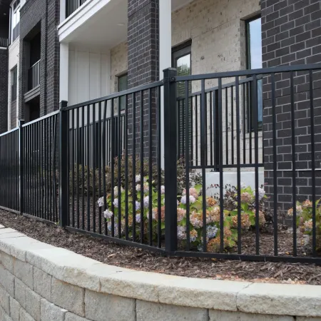 Black metal fence along a stone retaining wall in front of modern brick and stone townhouses with landscaping.
