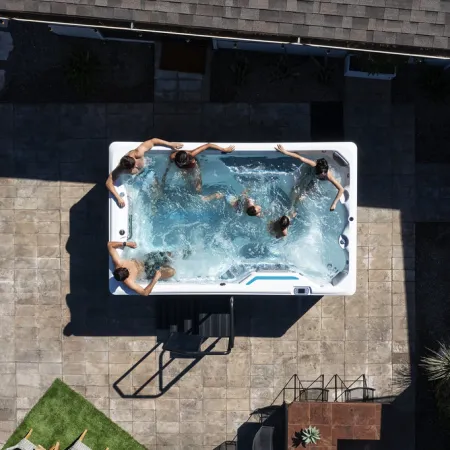 Aerial view of five people enjoying a jacuzzi hot tub on a patio with surrounding greenery and tiles.