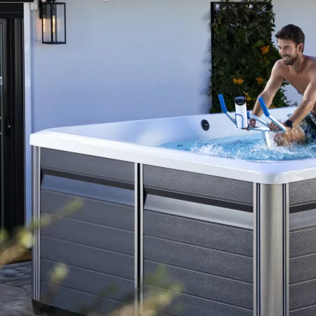 Man exercising on aquatic bike in a modern outdoor hot tub with gray panels and water jets.
