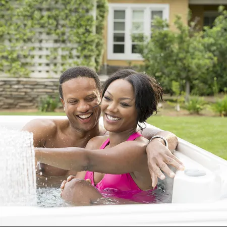 Happy couple enjoying relaxing time together in an outdoor hot tub with water fountain feature.