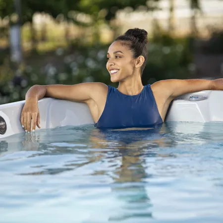 Smiling woman relaxing in a hot tub outdoors with arms resting on tub edge on a sunny day.