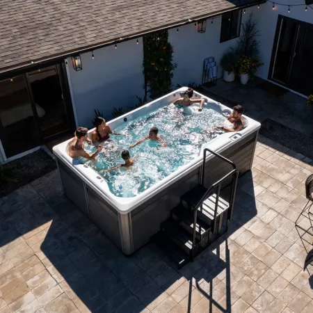 Family enjoying a large outdoor hot tub in a backyard patio with seating and plants around.