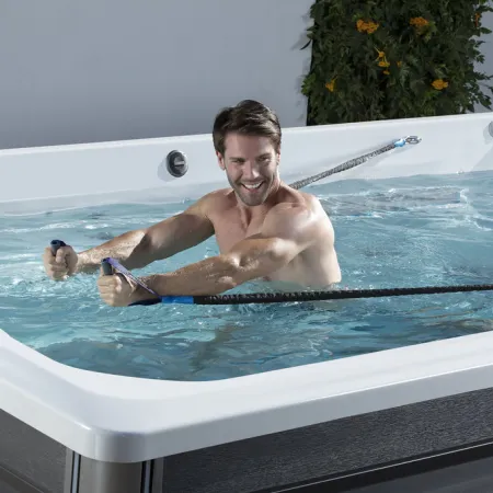 Man exercising with resistance bands in a modern swim spa filled with water, smiling during workout session