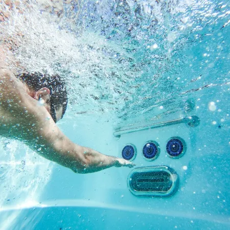 Man swimming underwater in a pool reaching toward three circular water jets and a vent on the pool wall.
