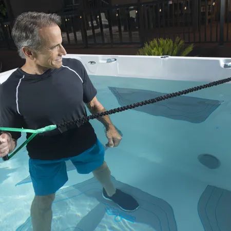Man in swimwear exercising with resistance cord in a backyard swim spa or pool.