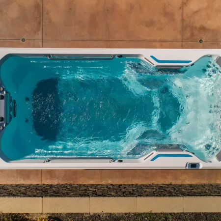 Top view of a rectangular outdoor swim spa with bubbling water on a tiled patio.