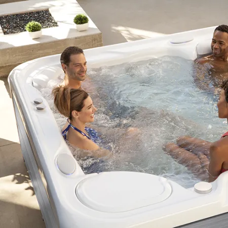 Four friends relaxing and chatting in a bubbling outdoor hot tub on a sunny patio.