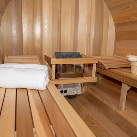 Wood-paneled sauna interior with wooden benches, a white towel, sauna heater, and a bucket with a brush.