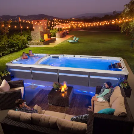 Outdoor evening scene with people relaxing in a hot tub and on patio furniture under string lights.