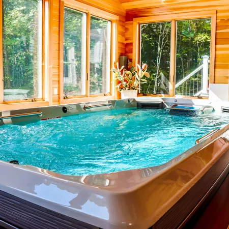 Indoor hot tub with clear blue water surrounded by large windows and wooden walls in a cozy room.