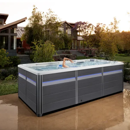 Modern swim spa with a swimmer inside set on a patio in a landscaped backyard at sunset.