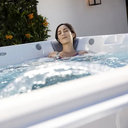 Woman relaxing in a bubbling outdoor hot tub with greenery and white walls in the background