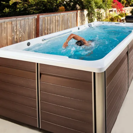Person swimming in a modern rectangular outdoor swim spa with wood panel design beside a wooden fence.