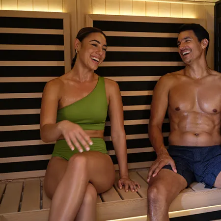 Smiling man and woman relaxing in a wooden sauna wearing swimwear, enjoying a heated steam room session