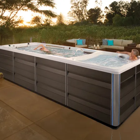 Outdoor swim spa with two people relaxing in water surrounded by patio furniture at sunset