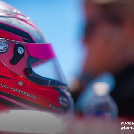 Close-up of a red racing helmet with black stripes and the name Ashton Harrison against a blurred background.