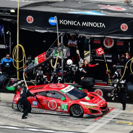 Red No. 93 race car in pit stop with crew changing tires and refueling under Konica Minolta signage