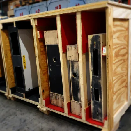 Wooden crates holding large vintage arcade game cabinets stored in an industrial warehouse setting