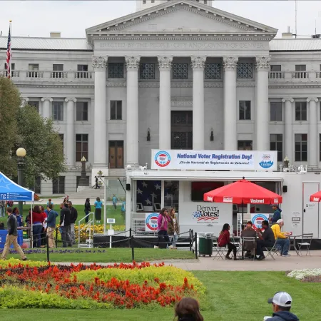 Outdoor National Voter Registration Day event with tents, people, and historic government building in background