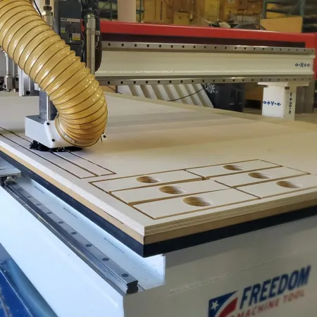 CNC router machine cutting rectangular wood pieces with holes in a woodworking workshop.