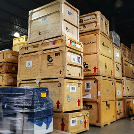 Warehouse stacks of large wooden crates and pallets wrapped in plastic under industrial lighting.